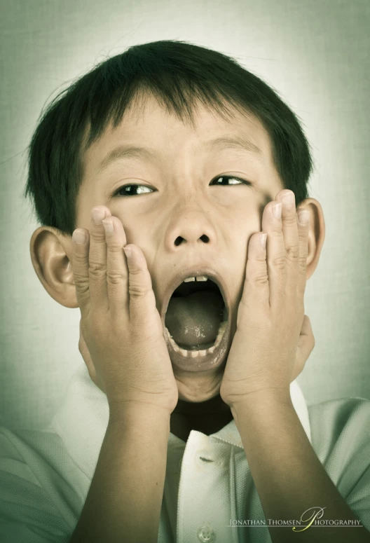 a young asian boy covering his face with his hands