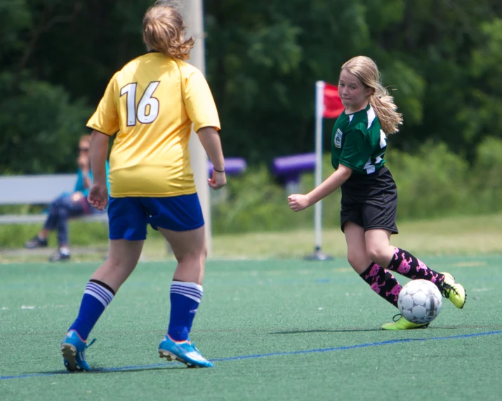 two women kicking around a soccer ball on the field