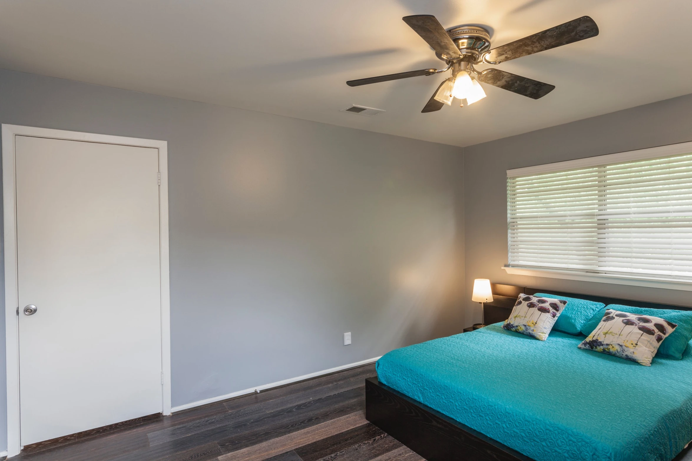 a bed sitting under a ceiling fan next to a lamp