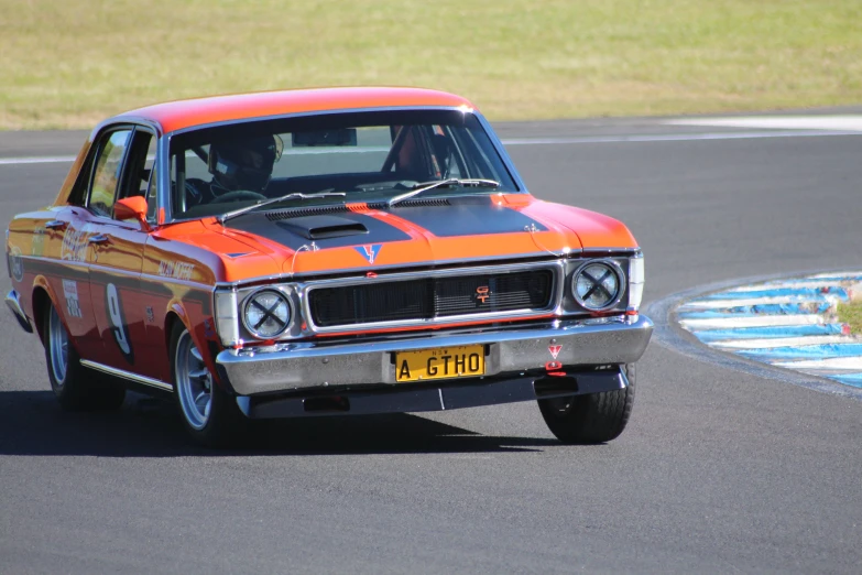 an orange muscle car drives down the track