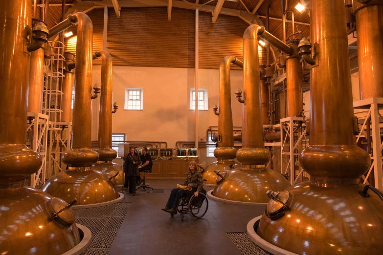 a man in wheel chair standing inside a building with huge gold metal pots