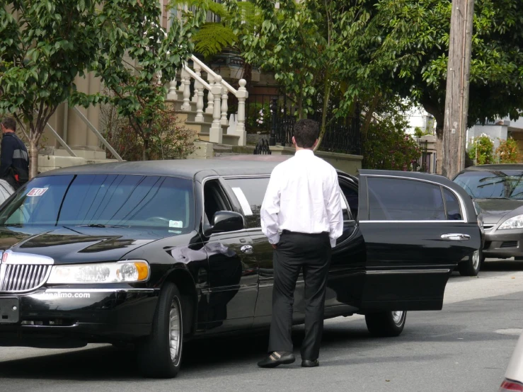 a black limousine and man with white shirt standing in the street