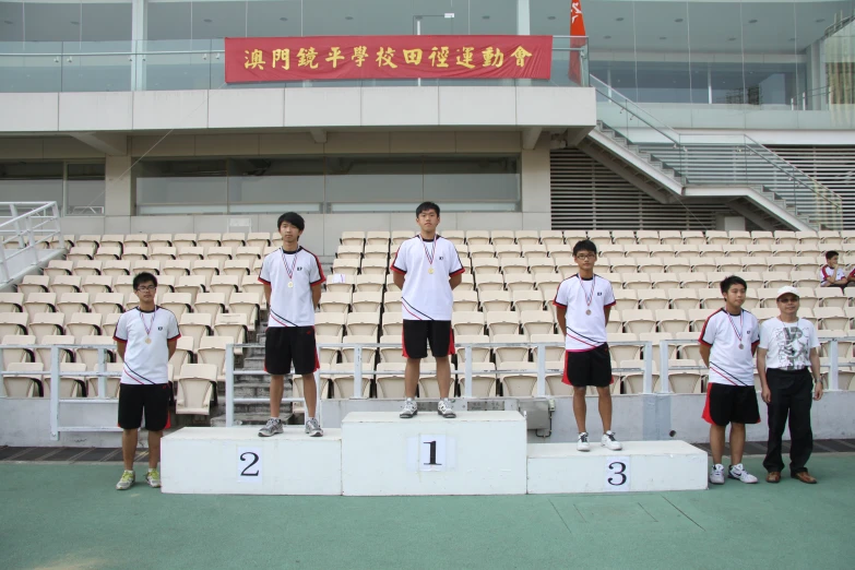 three boys are standing on a small podium in front of an empty stadium