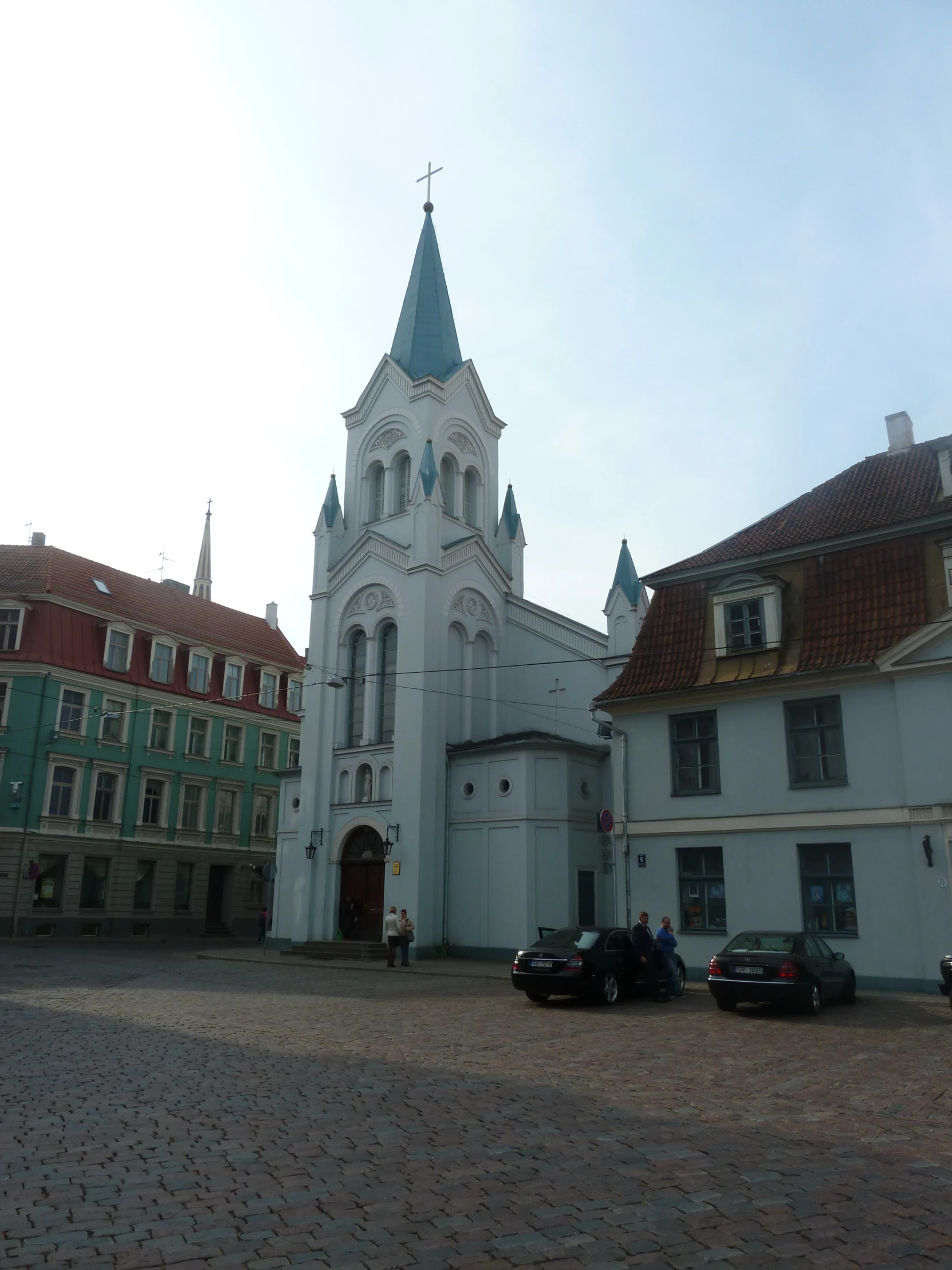 people walking outside a white church with red and green buildings