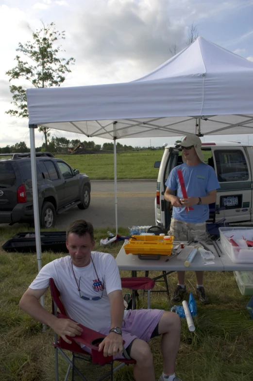 the two men are sitting in chairs under the tent