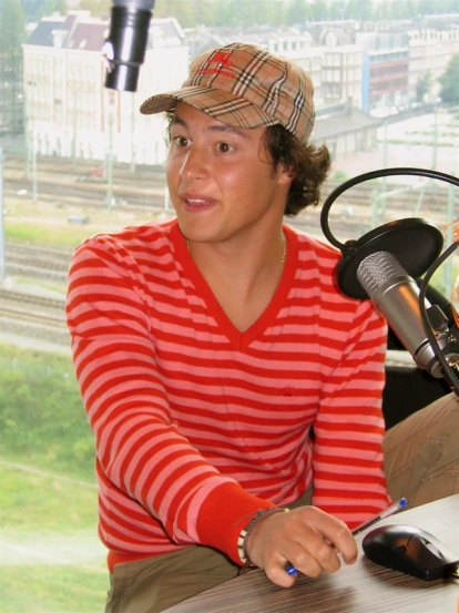 a young man in striped shirt sitting in front of a microphone