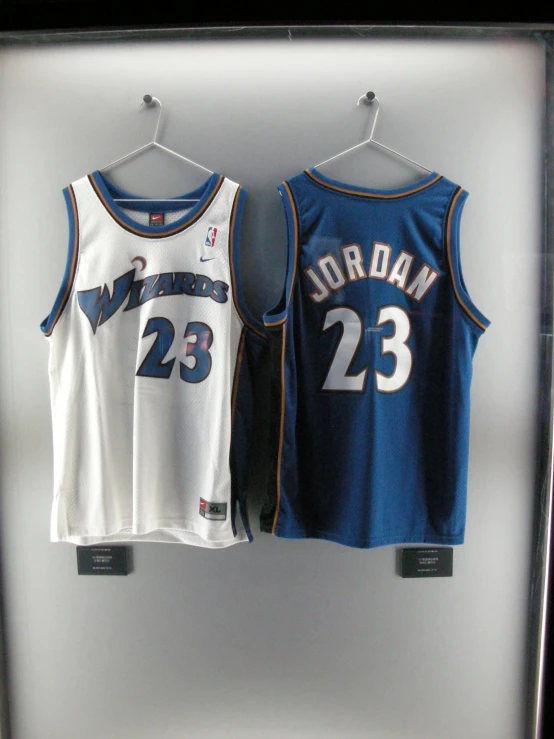 two basketball jerseys hang on a wall in a display case