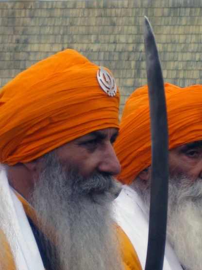 two men wearing orange turbans and holding an old staff