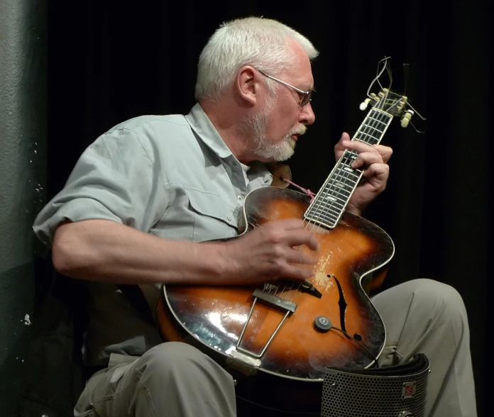 a man sitting in front of a microphone and holding an electric guitar