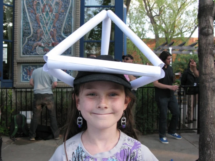 a girl stands wearing a hat made of paper