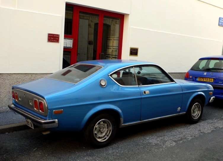 a blue car parked near a building and two other cars