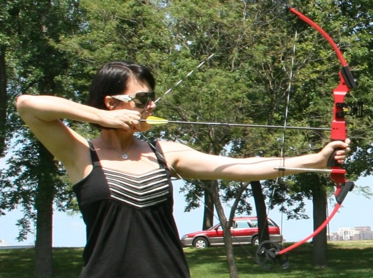 woman in sunglasses aiming a bow at the ground