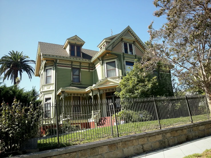 a large green victorian house with a black gate