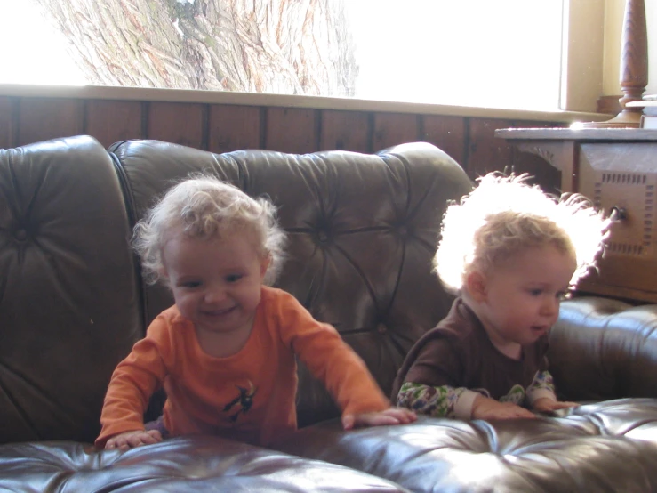 two little babies sitting in leather couches playing