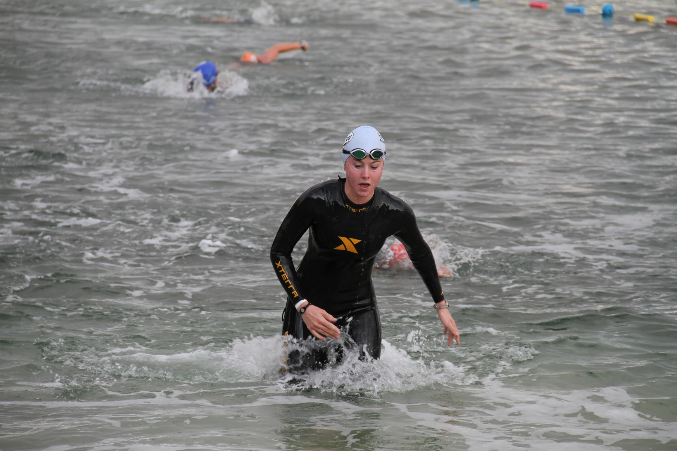 a man with a swimming suit and swim cap, standing in shallow water