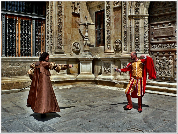 two men in medieval clothes standing near a building