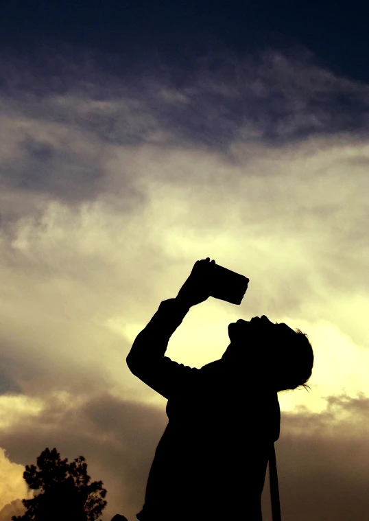 a man holding up his beverage against a cloudy sky