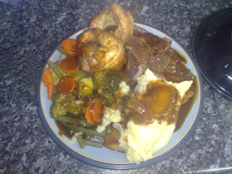a plate filled with meat, gravy, vegetables and potatoes