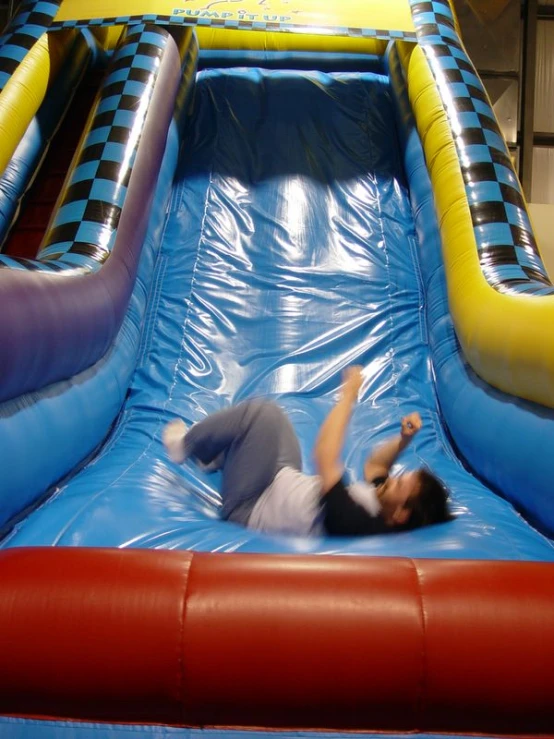 the boy in grey shorts is falling off of the inflatable slide