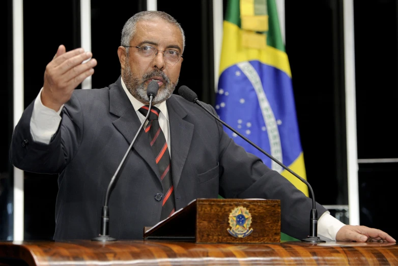 man at podium with flag in background giving speech