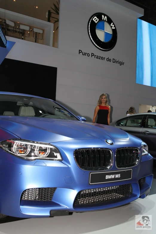 two blue bmws on display in front of a woman