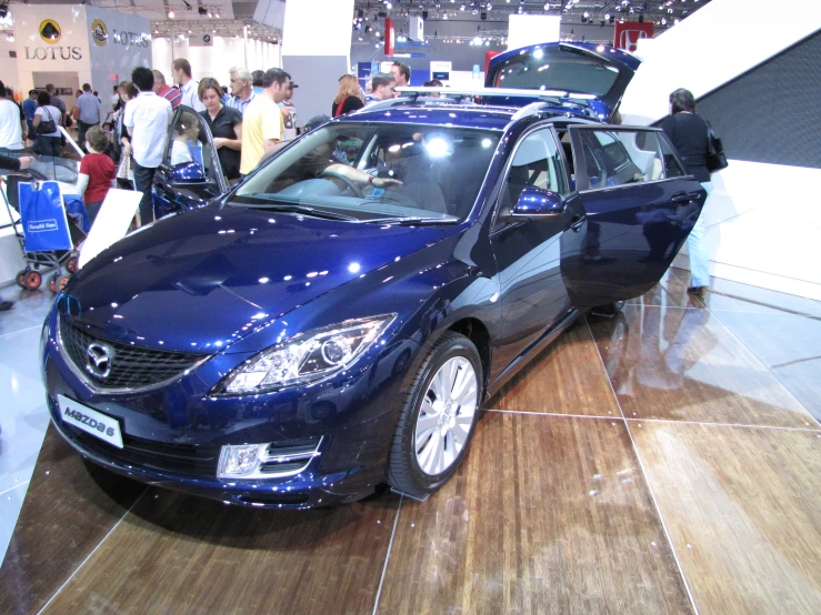 people are looking at a large blue car in a showroom