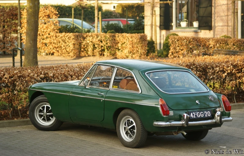 the classic car is green and parked next to the bushes