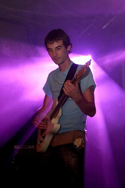 a young man playing a guitar while standing in front of purple light