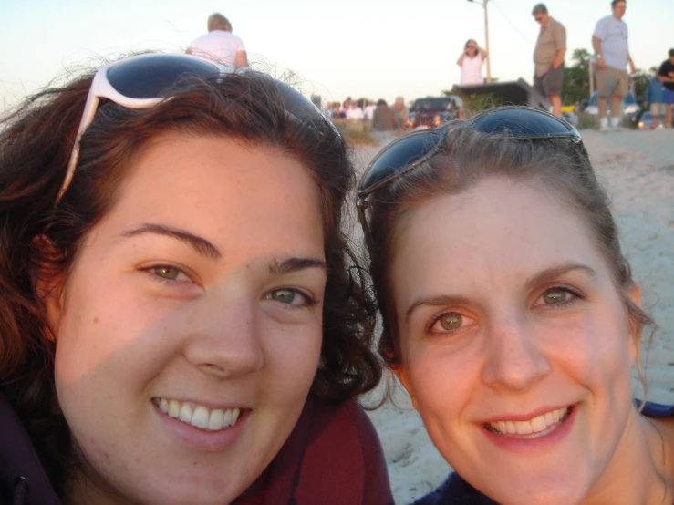 two women smiling and posing for the camera on the beach