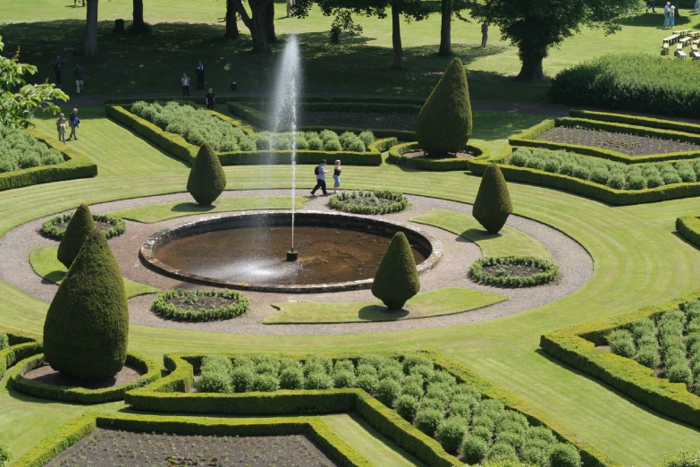 a fountain surrounded by formal garden landscaping, with people walking by