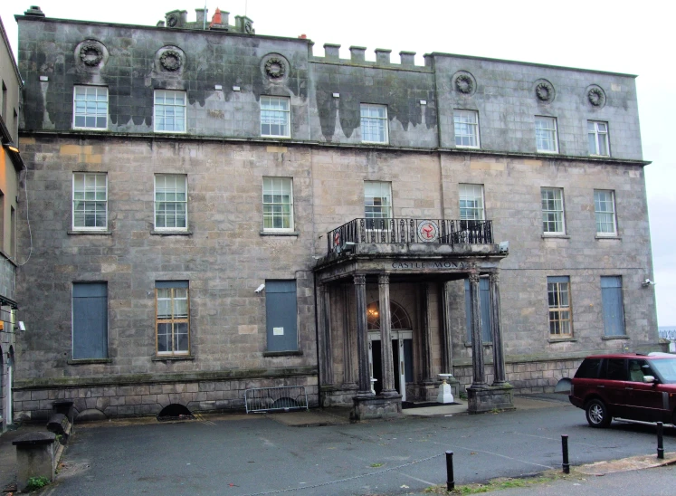 the exterior of an old stone building with a red car parked in front