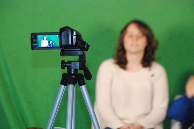 a woman standing next to a green screen holding a camera