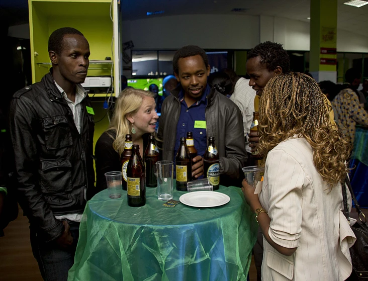 five people are standing around a table with bottles of beer