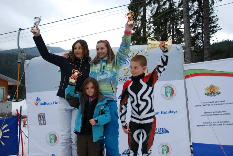 three children and one adult are posing with their ski gear