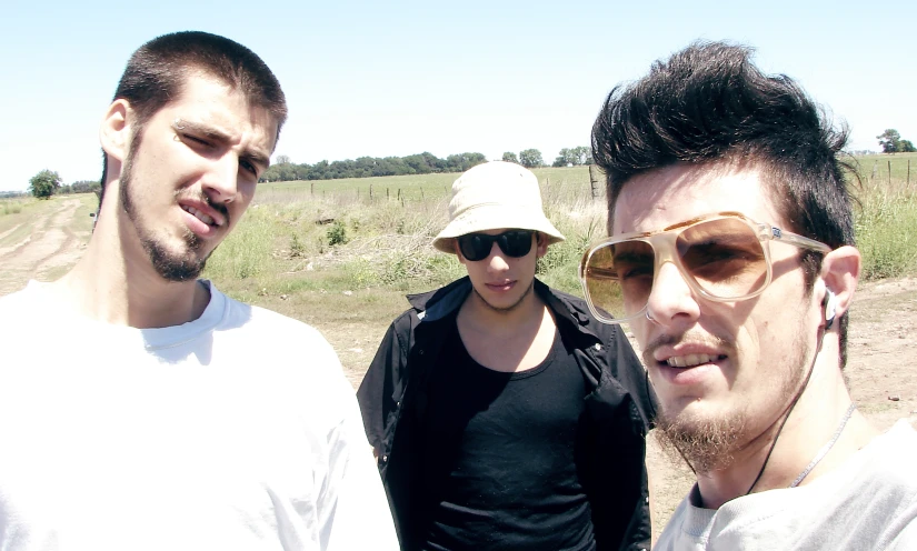 three men standing in the grass, one with sun glasses and the other with soing
