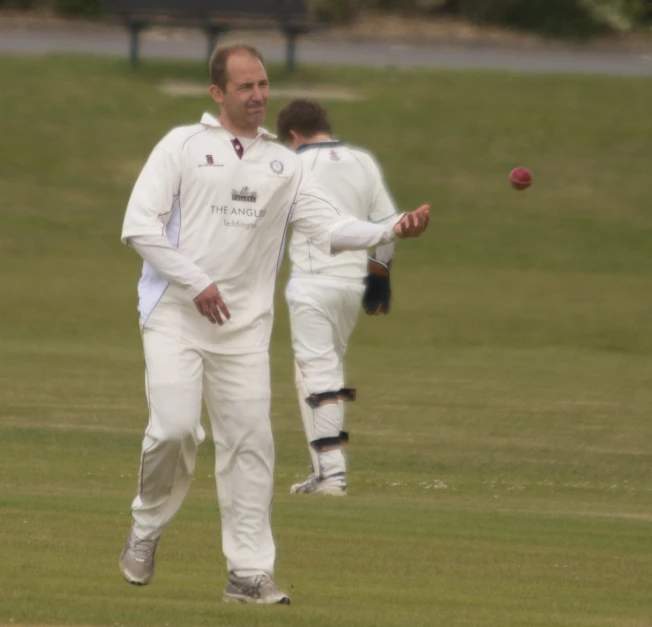 two men in white uniforms, both wearing gloves and one with a red ball in his hand