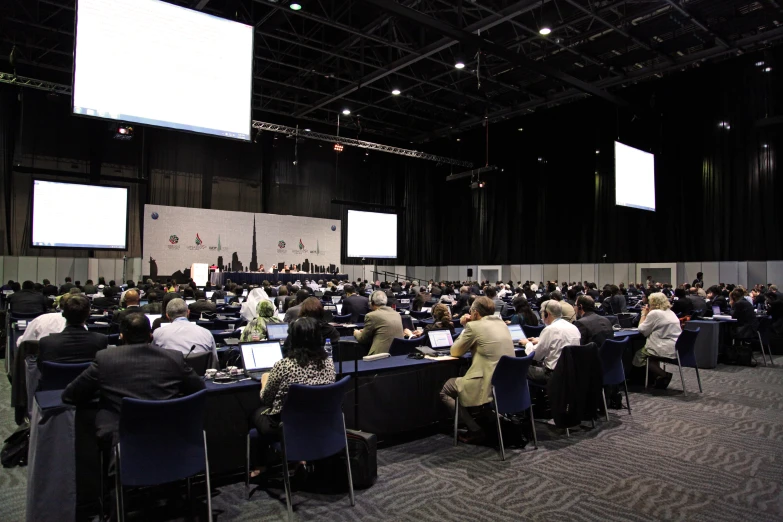 a group of people are sitting in an auditorium on laptops