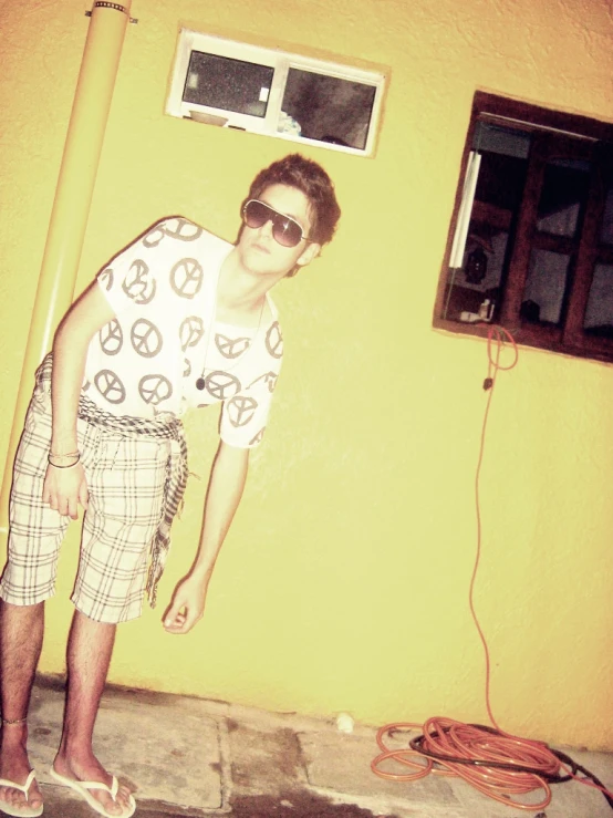 a young man stands on a concrete floor in front of a yellow wall