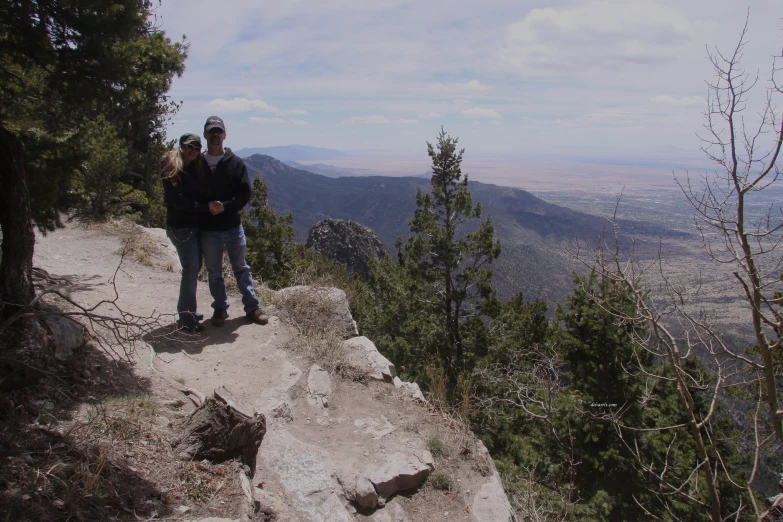 two people stand on a mountain near some trees