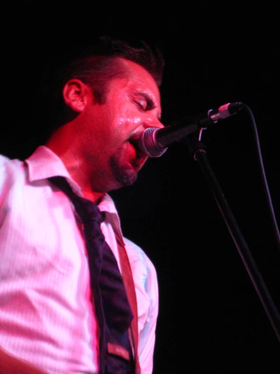 a man with an afro and a black tie on singing into a microphone