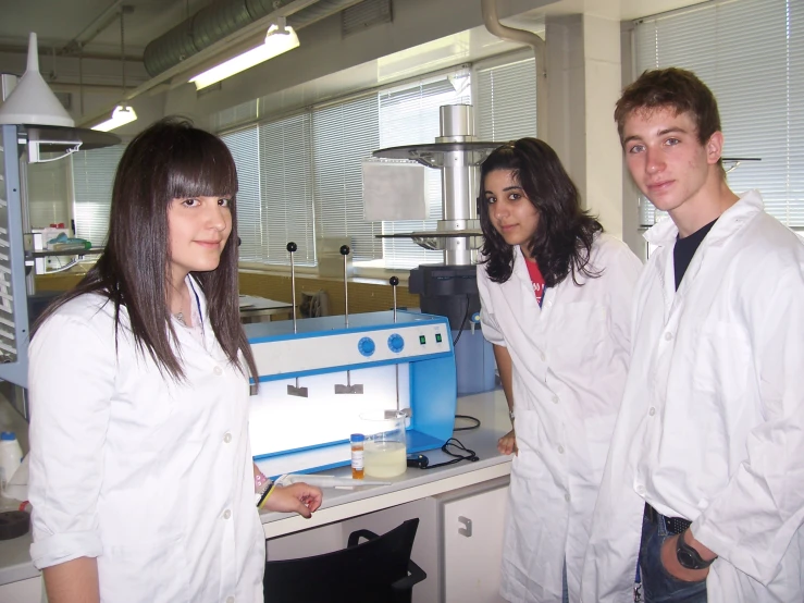 three people in lab coats standing near a machine