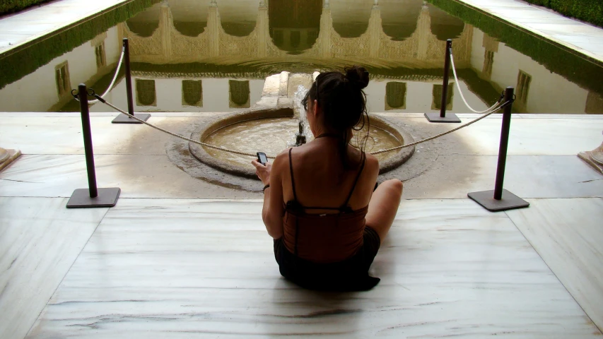 a woman sitting on the ground in front of a fountain