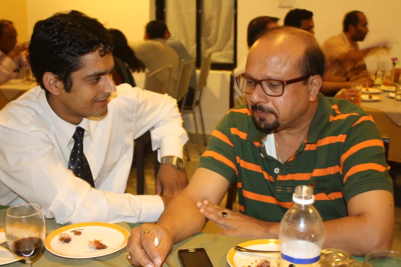 two men are seated at a table looking at each other