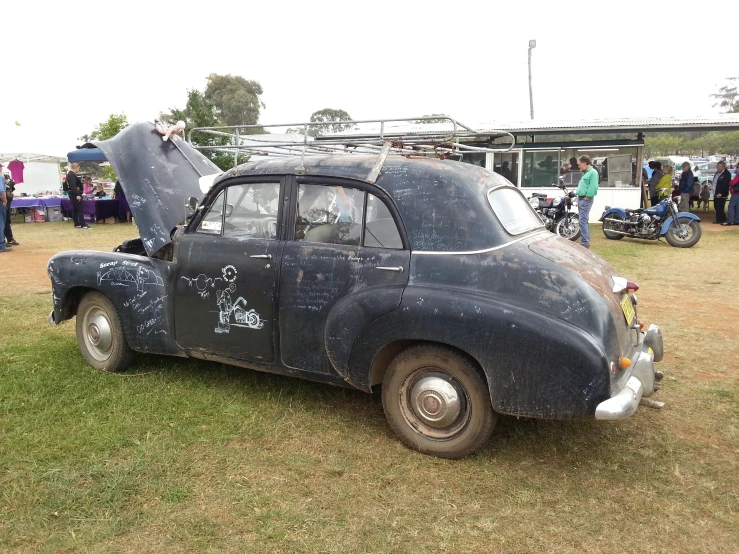 an old car with an open hood sitting on a grassy field