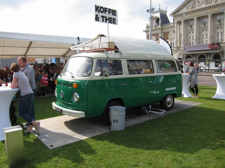 people are gathered in the grass near an old vw van