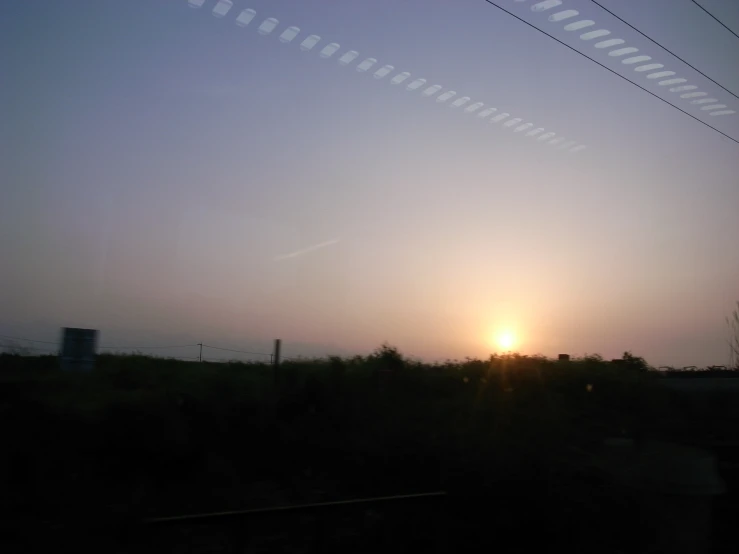 sun setting through some power lines with a sky background