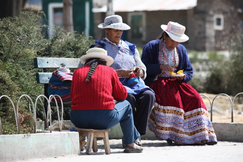 three people dressed up in mexican attire talking and sitting on a bench
