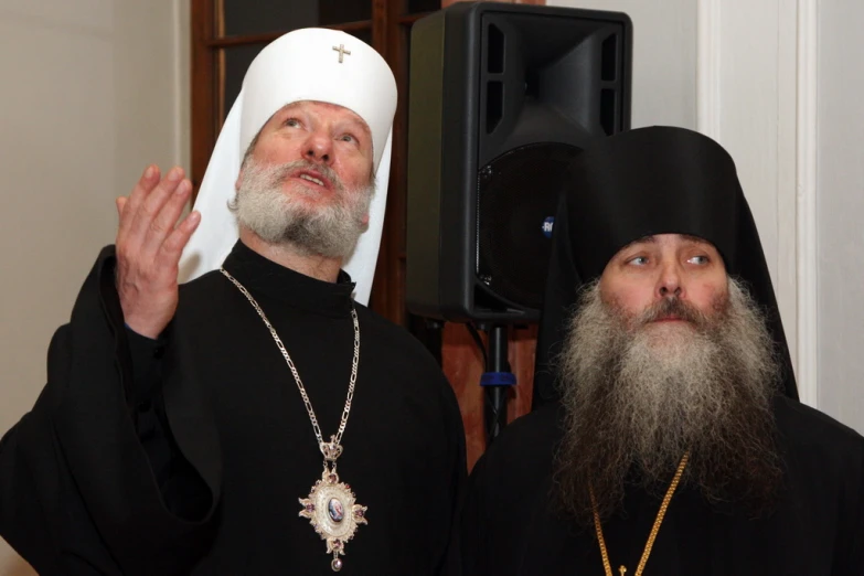 a priest wearing a large cross with his hands up to the side of a person in black robes