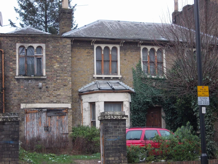 a brick house with many windows and an older red car