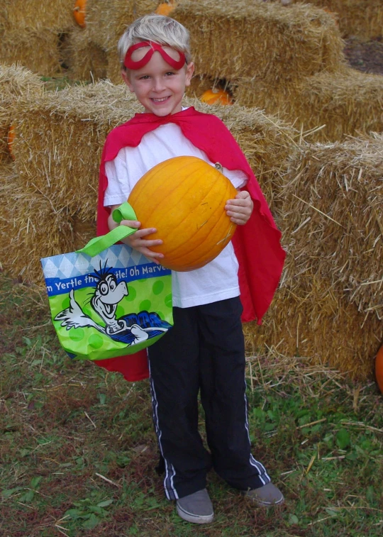 a boy is holding a pumpkin, some bags and a book